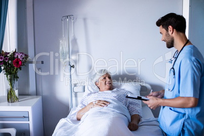 Male doctor discussing medical report with female senior patient on bed
