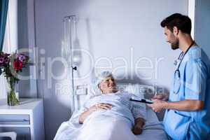 Male doctor discussing medical report with female senior patient on bed