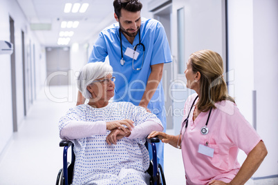 Male and female doctor interacting with female senior patient on wheelchair in corridor