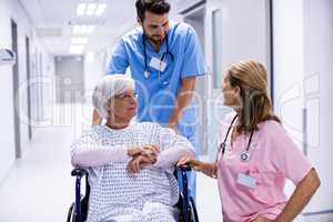 Male and female doctor interacting with female senior patient on wheelchair in corridor