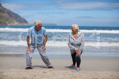 Senior couple doing stretching exercise on the beach