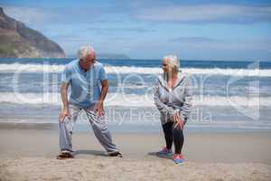 Senior couple doing stretching exercise on the beach