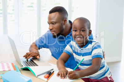 Father using laptop and son doing his homework in living room