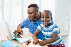 Father using laptop and son doing his homework in living room