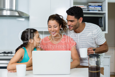 Parents and daughter using laptop in kitchen at home