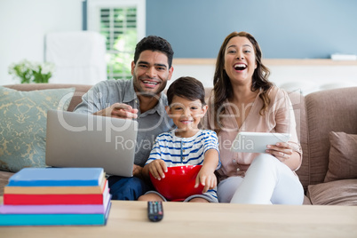 Son watching television while father and mother using laptop and digital tablet at home