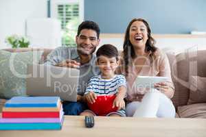 Son watching television while father and mother using laptop and digital tablet at home