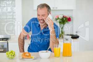 Man talking on mobile phone while having breakfast in kitchen
