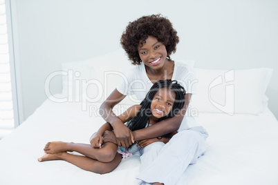 Smiling mother and daughter with arm around on bed