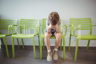 Upset boy sitting on chair in corridor