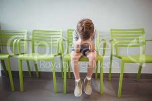 Upset boy sitting on chair in corridor