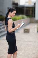 Happy businesswoman holding clipboard and using mobile phone