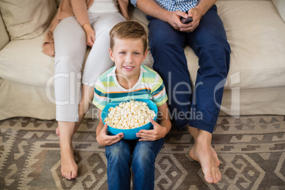 Portrait of boy sitting with bowl of popcorn in living room