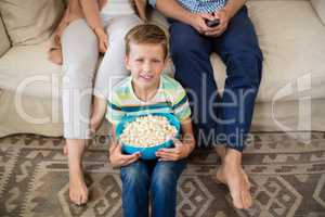 Portrait of boy sitting with bowl of popcorn in living room