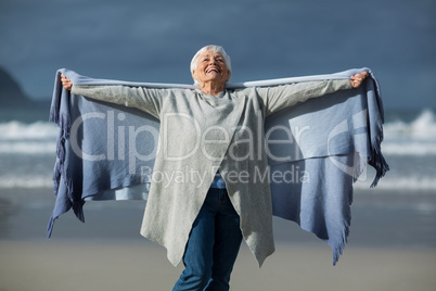Smiling senior woman wrapped in shawl at beach