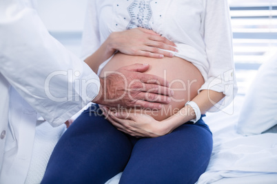Mid section of doctor touching pregnant womans belly in ward