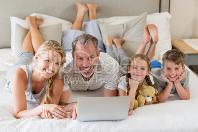 Parents with their kids lying on bed and using laptop in bedroom
