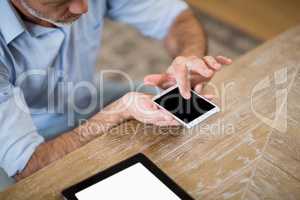Man using mobile phone with digital tablet on table in living room