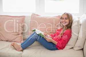 Smiling girl sitting on sofa and doing homework in living room