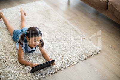 Girl using digital tablet while lying on rug in living room