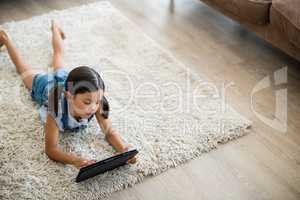 Girl using digital tablet while lying on rug in living room