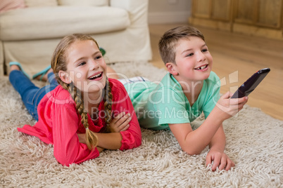 Siblings lying on rug and watching television in living room