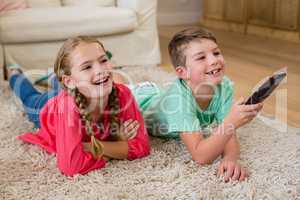 Siblings lying on rug and watching television in living room