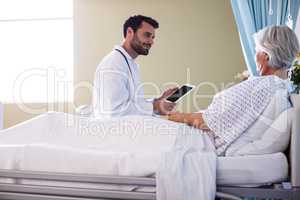 Male doctor discussing medical report over digital tablet with female senior patient in the ward