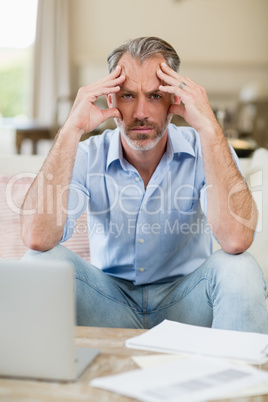 Worried man sitting on sofa with bills and laptop in living room