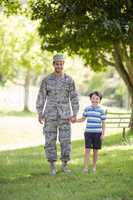 Portrait of army soldier holding hands of his son in park