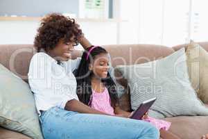 Mother and daughter sitting on sofa using digital tablet in living room