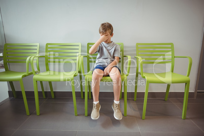 Upset boy sitting on chair in corridor