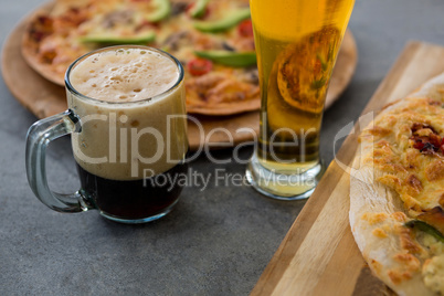 A mug of beer and glass with pizza in the background