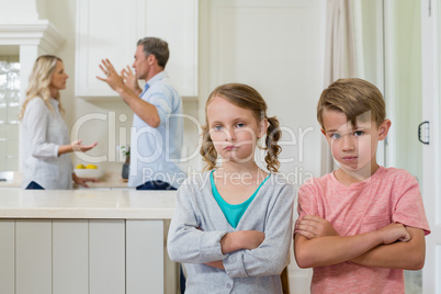 Sad sibling standing with arms crossed while parents arguing each other