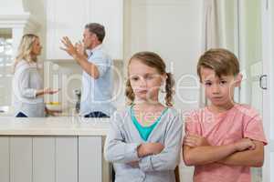 Sad sibling standing with arms crossed while parents arguing each other