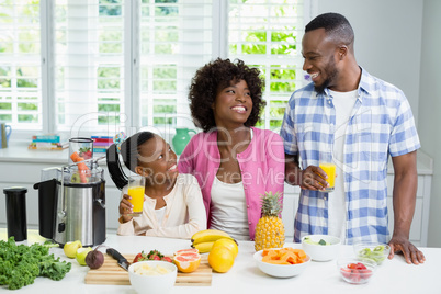 Smiling parents and daughter having a glass of orange juice in kitchen at home