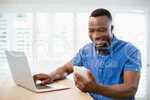 Man using laptop and mobile phone in living room