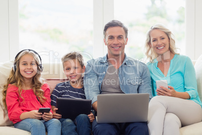 Portrait of parents and kids sitting on sofa with laptop, mobile phone and digital tablet