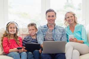 Portrait of parents and kids sitting on sofa with laptop, mobile phone and digital tablet