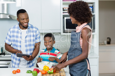 Mother and son preparing salad while father using digital tablet in kitchen