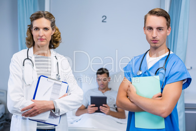 Doctors standing with reports and patient using digital tablet in background