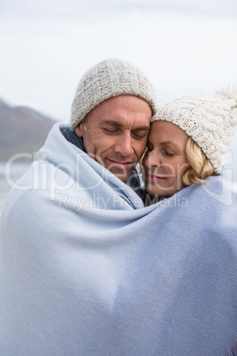 Mature couple wrapped in blanket on the beach