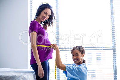 Portrait of doctor measuring pregnant womans belly in ward