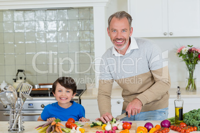 Portrait of son and father chopping vegetables in kitchen