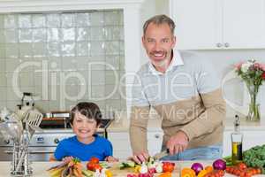 Portrait of son and father chopping vegetables in kitchen