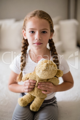 Girl holding a teddy bear on bed in bedroom