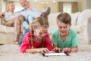 Sibling lying on rug and using digital tablet in living room