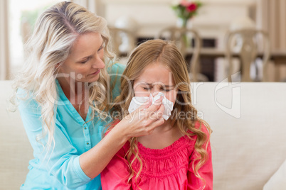 Mother helping daughter blowing her nose on sofa