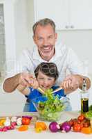 Smiling father and son preparing salad in kitchen at home