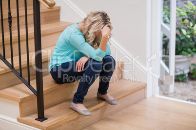 Tense woman sitting on staircase with hand on forehead
